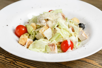 Chicken caesar salad with lettuce leaves in white bowl on wooden table