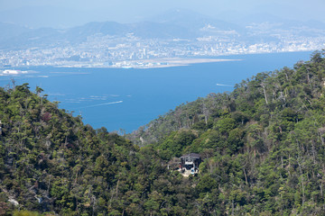Fototapeta premium Big gondola starts to lift from the Kayatani stop of ropeway to the peak of mount Misen. Aerial view from cabin at the sea, virgin forests and Hiroshima city. Itsukushima, Japan