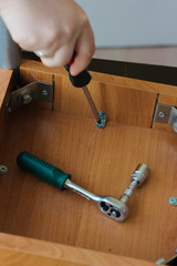 Hands screwing the screw to a wooden chair with the screwdriver.