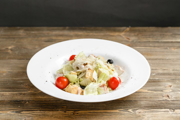 Chicken caesar salad with lettuce leaves in white bowl on wooden table