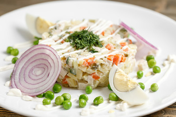 Olivier salad with trout in a white plate. Traditional Russian dish. Wooden background