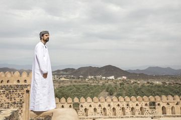arab man in traditional omani outfit overlooking the view of Omani countryside