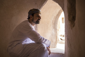arab man in traditional omani outfit looking out of a window in an old Omani castle