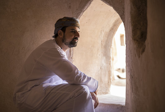 Arab Man In Traditional Omani Outfit Looking Out Of A Window In An Old Omani Castle