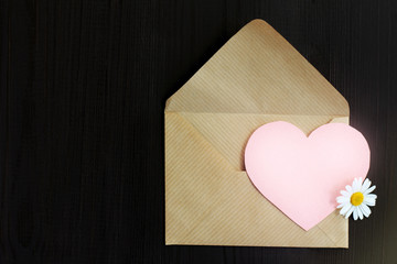 romantic message/ open paper envelope with a heart symbol and chamomile on a dark wooden surface top view