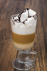 Tall glass with latte and marshmallow on wooden table