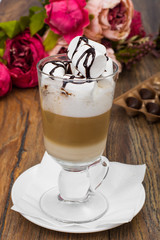 Tall glass with latte and marshmallow on wooden table