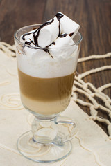Tall glass with latte and marshmallow on wooden table
