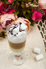 Tall glass with latte and marshmallow on wooden table