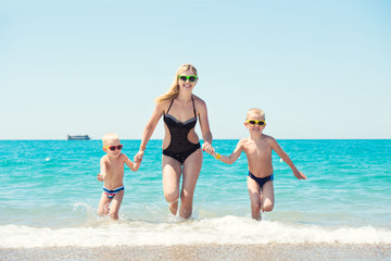 Beautiful mother and two lovely son holding hands running on the waves.Fun,family-friendly summer vacation.