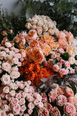 Naklejka premium Fresh flower delivery at the florist shop: different flowers stocked up together, orange red and paster colours; different types of roses and ranunculus with eucalyptus on the background