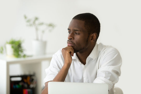 Young african-american thoughtful businessman holding hand on chin planning future project at work with laptop, black meditative african entrepreneur thinking of new idea for business improvement