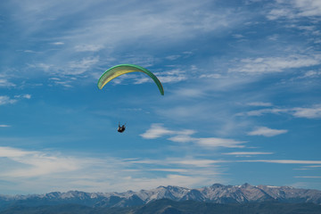 Paraglider green color flying high with snowy mountains background
