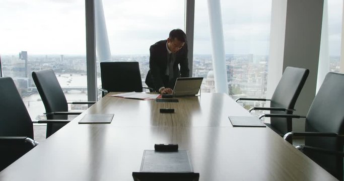 4K Worried businessman working alone in office boardroom, pacing in front of the window with city view in background