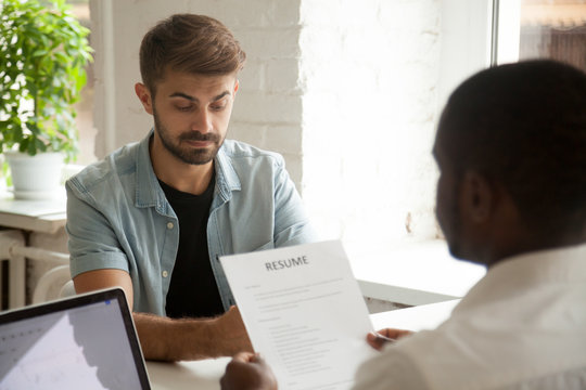 Stressed caucasian applicant feels worried while african hr employer reading resume, stress at job interview concept, nervous anxious man candidate waiting for result at hiring employment negotiation