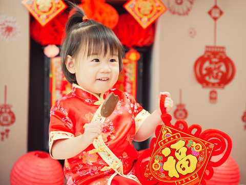 Chinese baby girl  with traditional dressing up and "FU" means "lucky" greeting card.some "FU" means "lucky"greeting card on the wall as well