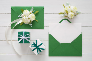 Wedding invitation cards or Valentines Day letters in green envelopes decorated with white rose flowers and two gift boxes. Flat lay. Top view. Copy space for text.