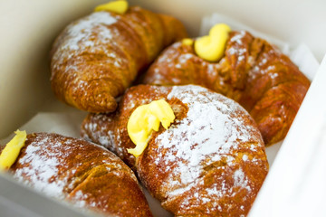 4 croissants with yellow egg cream and sugar powder in a white box for take away. Daylight. Traditional French and Italian breakfast