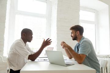 Multiracial businessmen negotiate discuss project talking at work, african and caucasian colleagues brainstorm new idea in office, black entrepreneur explaining corporate teamwork to white coworker