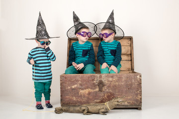Happy children in elegant green clothes play at home with a stuffed crocodile. Boys in carnival glasses and a hat are posing for a fashion magazine