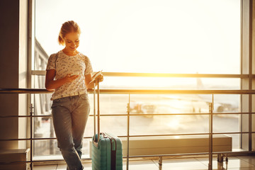 young woman waiting for flying at airport at window with suitcase