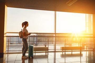 young woman waiting for flying at airport at window with suitcase  .