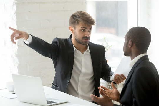 Angry rude caucasian executive firing male incompetent african employee for bad work, impolite white partner telling black businessman to get out detecting fraud, prejudice and racial discrimination