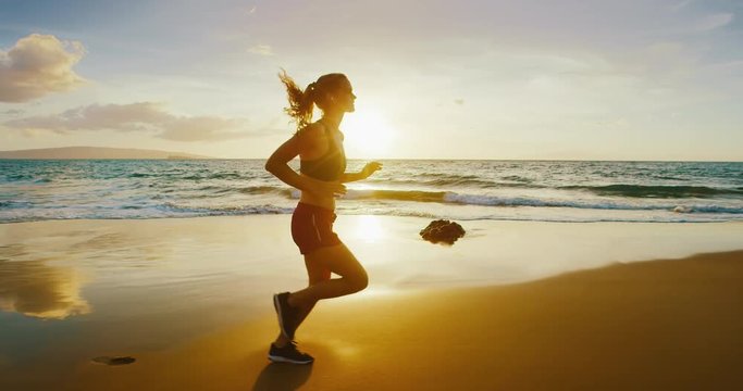 Athletic young woman running on the beach at sunset
