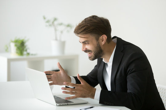 Happy surprised businessman in suit looking at laptop screen excited by online project result, successful entrepreneur sitting at office desk celebrating good news in email, motivated by business win