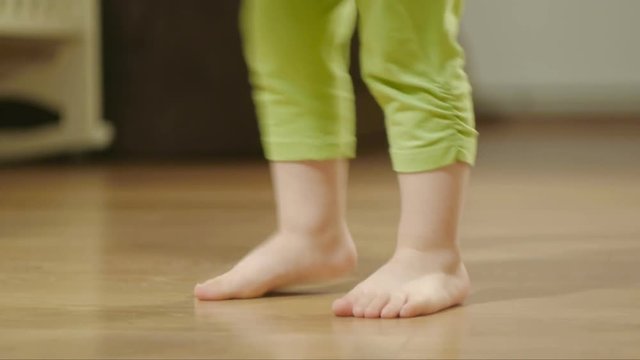 Closeup of the legs of a young child dancing and stomping on a wooden floor in a room