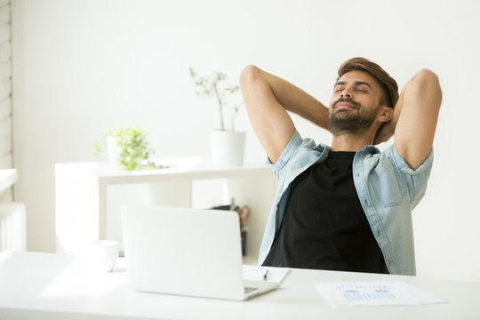 Relaxed young man resting from work on laptop holding hands behind head, successful entrepreneur relaxing feels happy breathing fresh air, smiling man enjoy break stretching in home office workplace