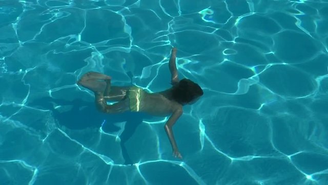 Girl swimming underwater in a pool. She pushes away from the pool wall with her feet