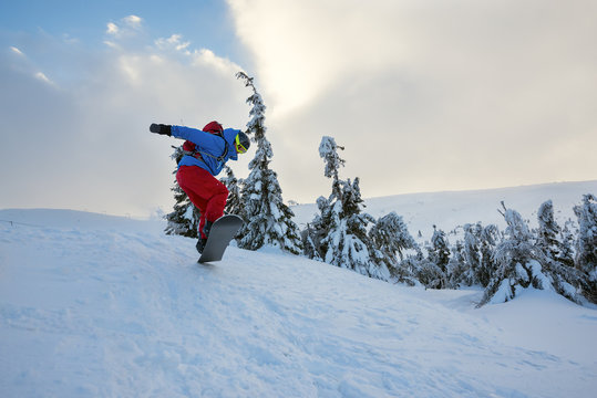 Snowboarder is jumping among snow covered fir trees