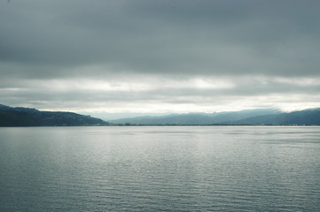 A stormy sky over a lake. The sun is breaking through the clouds, turning the water silver. The scene is deserted.