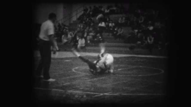 Archival footage of two young unrecognizable men wrestling near an official