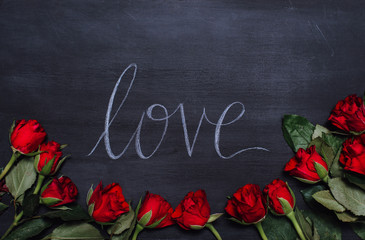 Fototapeta na wymiar Close up of flatlay on black wooden chalk board with the hand lettered word love in script font for Valentine's Day framed by red rose petals as symbol for love