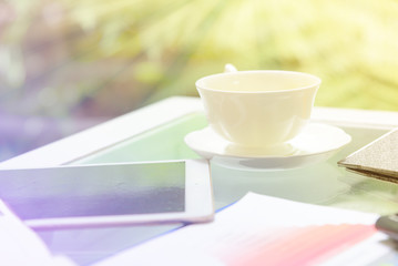 Workplace with digital tablet pc and cup of coffee on table with business worksheet  in the garden, morning time