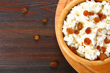 Homemade cottage cheese with almonds and raisins in a bowl on a wooden table.