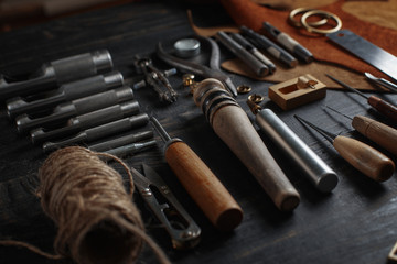 Set of leather craft tools on wooden background. Workplace for shoemaker. Piece of hide and working handmade tools on a work table.