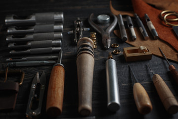 Set of leather craft tools on wooden background. Workplace for shoemaker. Piece of hide and working handmade tools on a work table