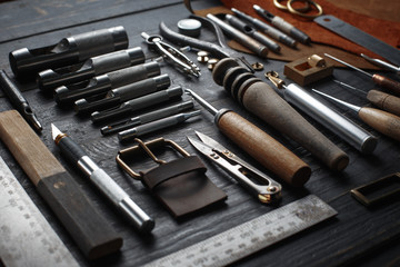 Set of leather craft tools on wooden background. Workplace for shoemaker. Piece of hide and working handmade tools on a work table