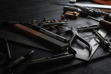 Set of leather craft tools on wooden background. Workplace for shoemaker. Piece of hide and working handmade tools on a work table