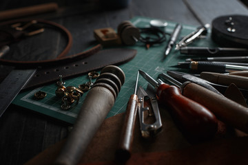 Set of leather craft tools on wooden background. Workplace for shoemaker. Piece of hide and working handmade tools on a work table