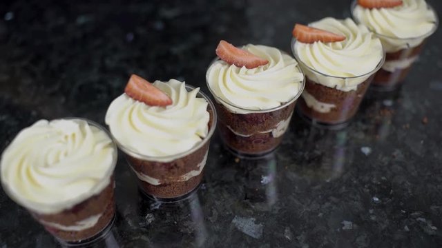 On kitchen table chocolate dessert is decorated with a strawberry. Hands in gloves are placed on top of sweet treat from crumbs with cream pieces of fresh berries for apetit. slowmotion slow motion