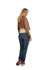 Obraz premium full length portrait of girl wearing brown leather jacket and jeans. standing pose facing away from the camera.