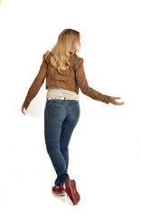 full length portrait of girl wearing brown leather jacket and jeans.   standing pose facing away from the camera.