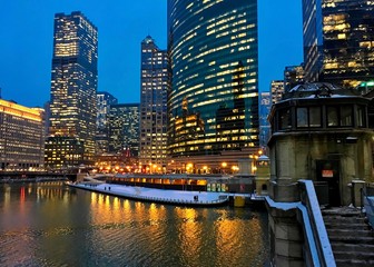 Obraz premium City night lights illuminate on a nearly frozen Chicago River as elevated train passes over snow covered Lake Street. Stairs lead to river bridgehouse.