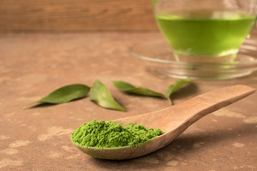 Close up of green tea powder in wooden spoon on the table with glass cup of hot tea background.