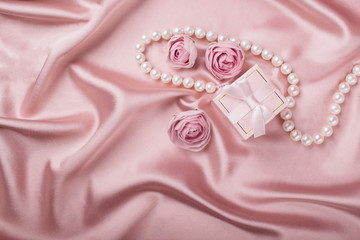 A gift box on a satin background is decorated with flowers and pearls. Copy space. Flat layout.