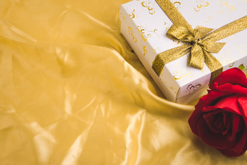 Gift box and red roses on golden fabric background. Free space for text